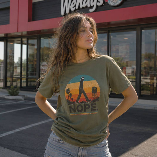 Woman wearing a t-shirt with a graphic fresno nightcrawler design and the word 'NOPE' in front of a Wendy's restaurant.