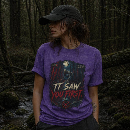 Person wearing a purple t-shirt with a rake graphic design and text in a forest setting