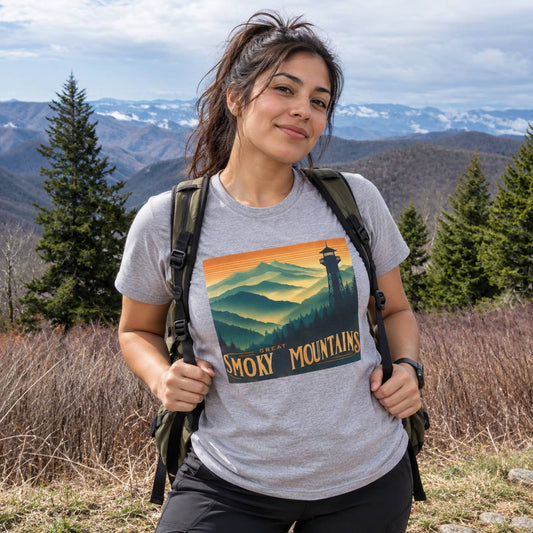 A woman wearing a heather gray t-shirt with a retro-style 'Smoky Mountains' mountain landscape graphic, photographed outdoors in a mountain setting with a backpack.