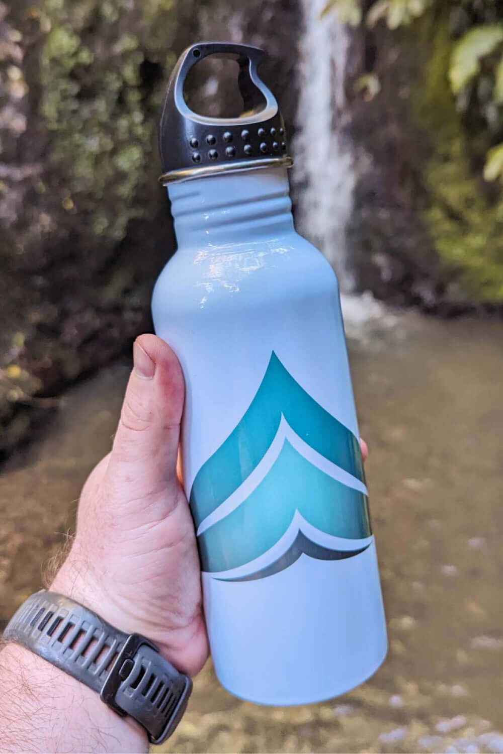 Wyld Peak stainless steel water bottle in the foreground with a small cascading waterfall behind it