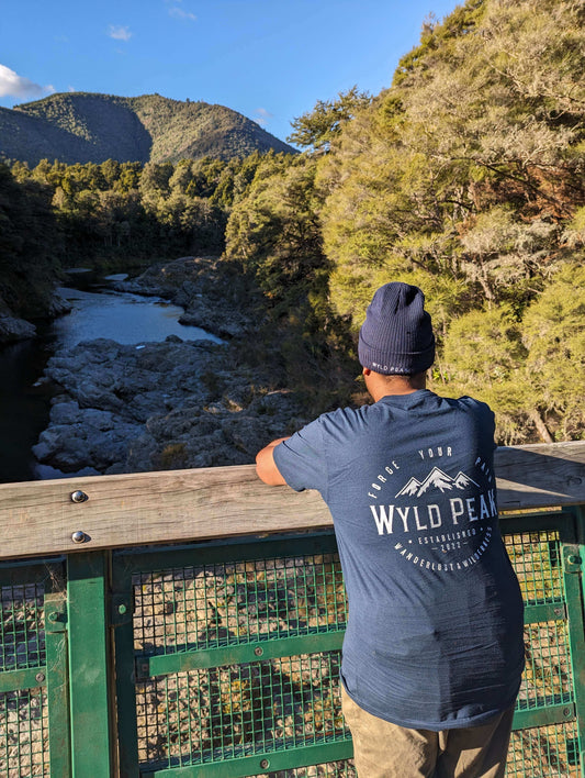 Avi standing on the scenic Pelorus Bridge in a Wyld Peak tee, surrounded by lush New Zealand forest and river views