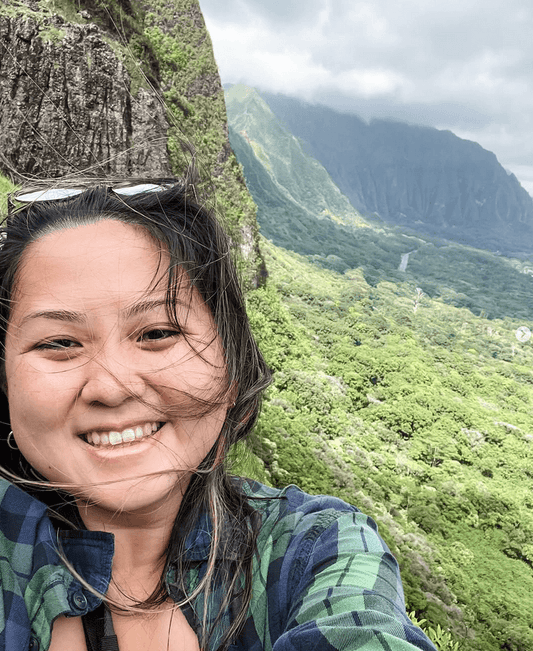 Ali (owlsaur) standing at a scenic trail viewpoint overlooking Honolulu, surrounded by lush greenery and ocean views