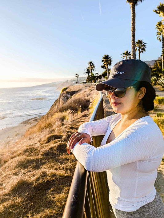 Mexican woman standing on the San Pedro cliffs in a Wyld Peak signature cap—adventuring with ocean views and coastal breeze