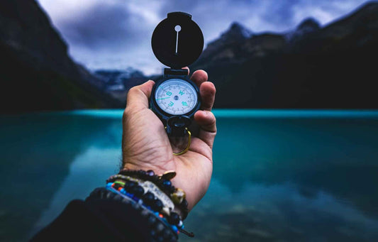 Hand holding a compass overlooking a lake and surrounding mountain valley, symbolizing direction in nature