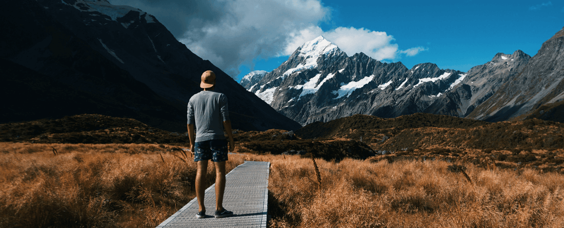 Hiker enjoying a sunny summer day on a scenic trail near Aoraki Mount Cook, New Zealand, with mountains in the background