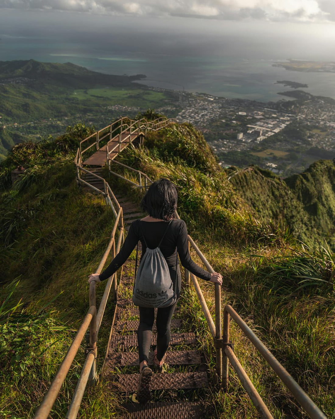 Female hiker descending a lush stair-step trail in Hawaii—tropical trekking adventure