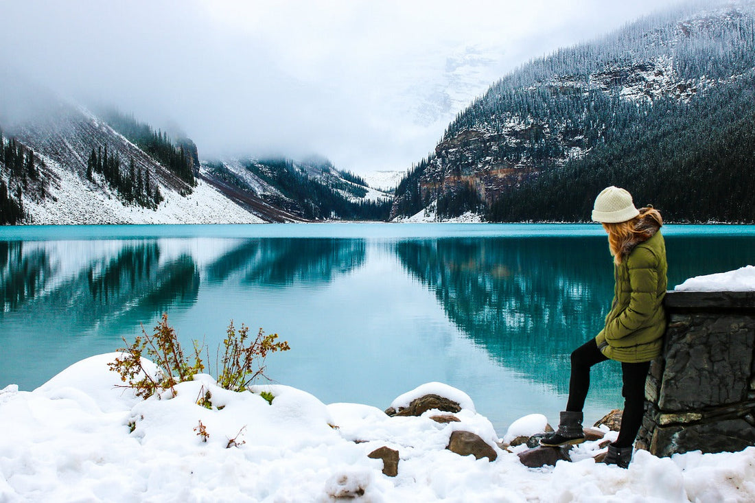 Woman hiker standing beside a frozen lake in a snow-covered mountain valley, embracing winter wilderness