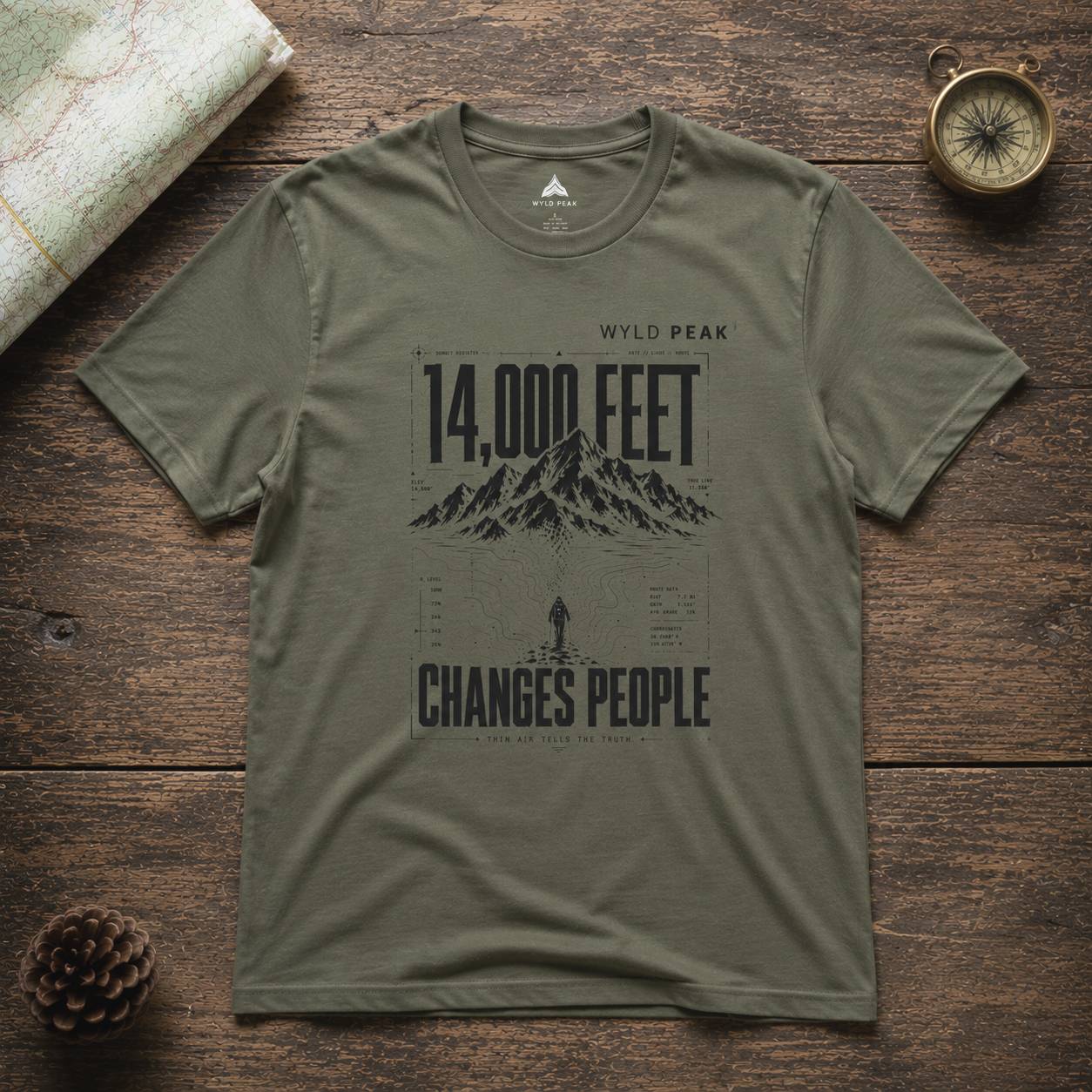 Green t-shirt with mountain graphic and text on a wooden surface
