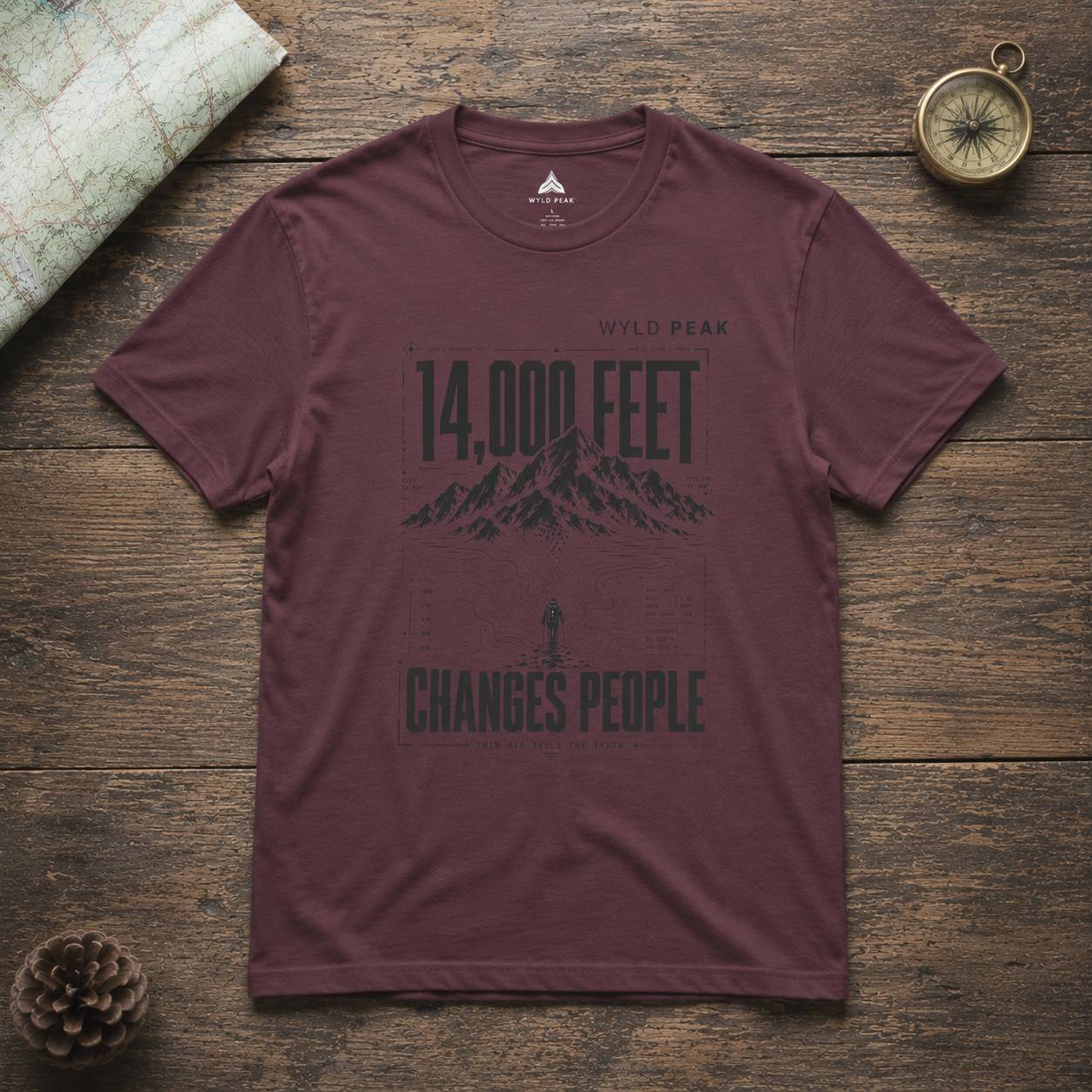 Maroon t-shirt with mountain graphic and text on a wooden surface