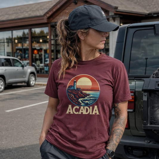 Person wearing a maroon t-shirt with 'Acadia' design standing next to a vehicle.