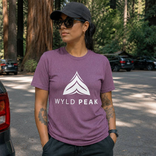 Person wearing a purple 'Wyld Peak' t-shirt in a forested area.