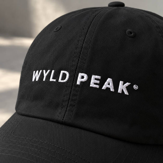 A close-up of a black baseball cap with 'WYLD PEAK' embroidered in white across the front panels.