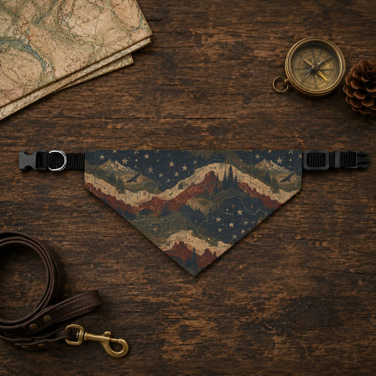 Dog bandana with mountain design on a wooden surface with map, compass, and pine cone.