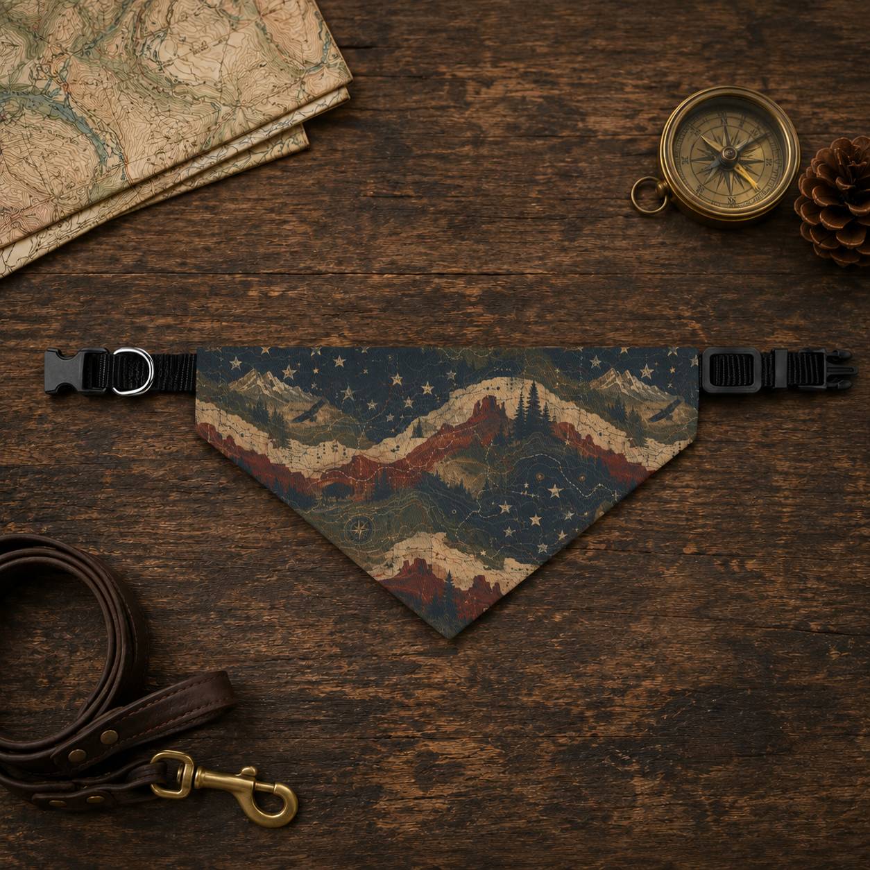 Dog bandana with mountain design on a wooden surface with map, compass, and pine cone.