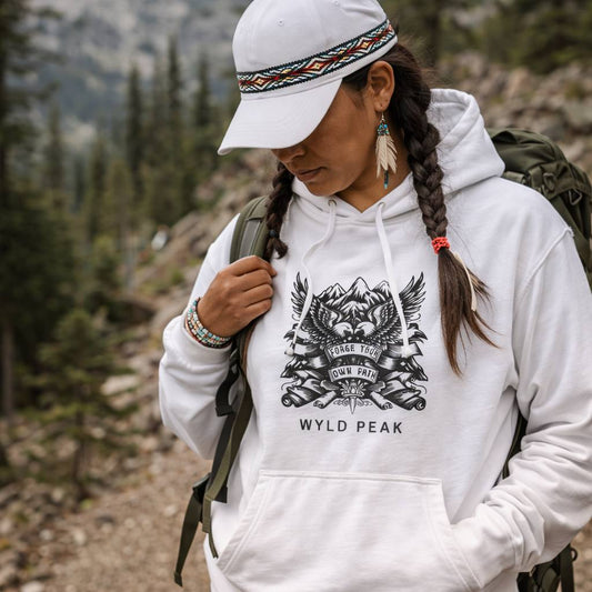 Person wearing a white hoodie with a logo and text, standing in a mountainous area.