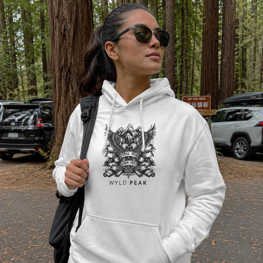 Woman wearing a white hoodie with a logo and text in a forest setting