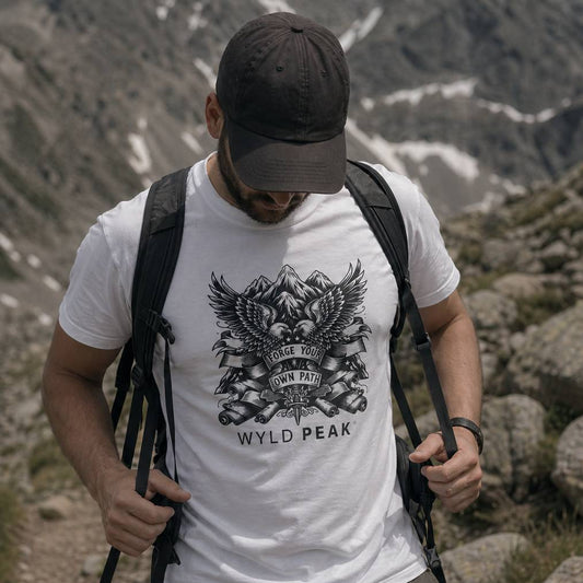 Man hiking in a mountainous area wearing a white t-shirt with 'Wyld Peak' branding.
