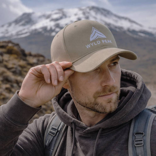 Man wearing a beige cap with 'Wyld Peak' logo against a mountainous background