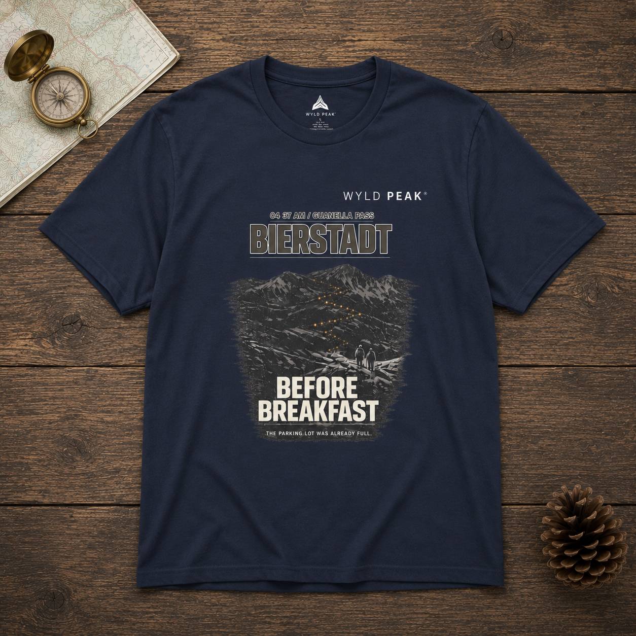 Navy blue t-shirt with mountain graphic and text on a wooden surface with map and compass.