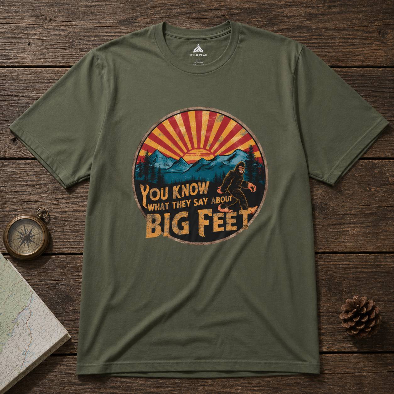Green t-shirt with a bigfoot graphic design on a wooden surface