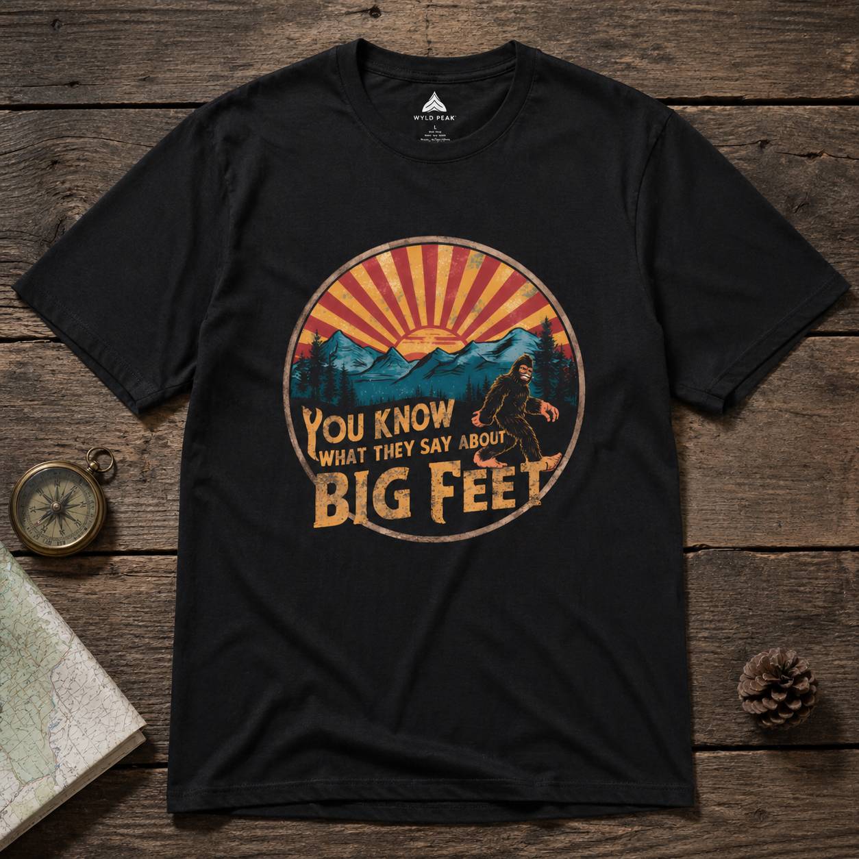Black t-shirt with a mountain and bigfoot graphic on a wooden surface