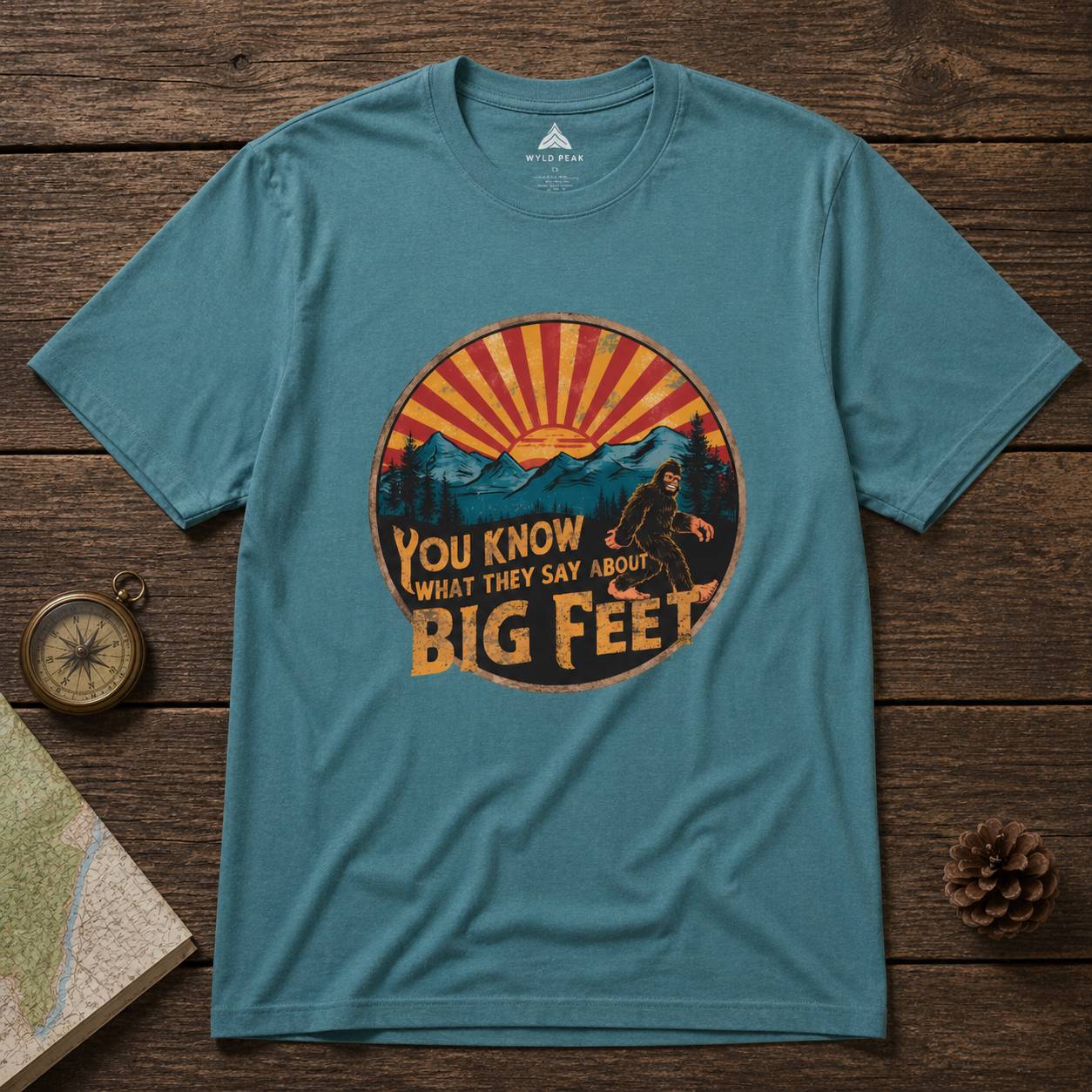 Blue t-shirt with a bigfoot graphic design on a wooden surface