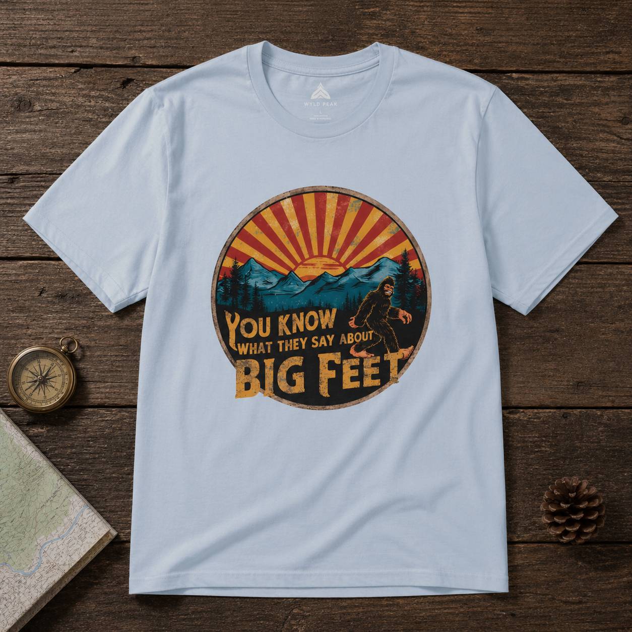 Light blue t-shirt with a bigfoot graphic design on a wooden surface