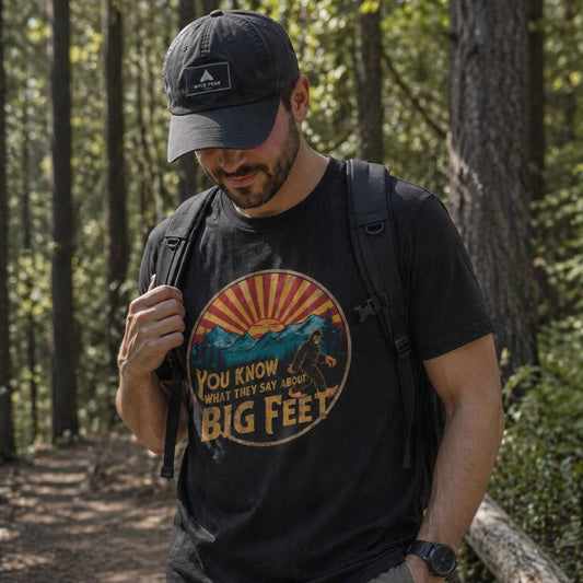 Man in a forest wearing a black t-shirt with a graphic design and text, holding a backpack.
