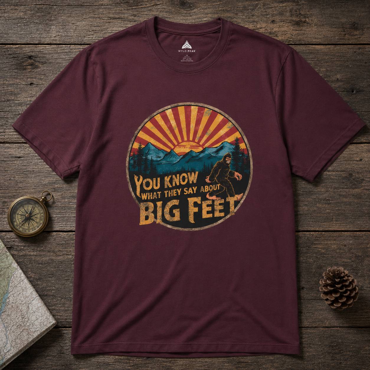 Maroon t-shirt with bigfoot graphic design on a wooden surface
