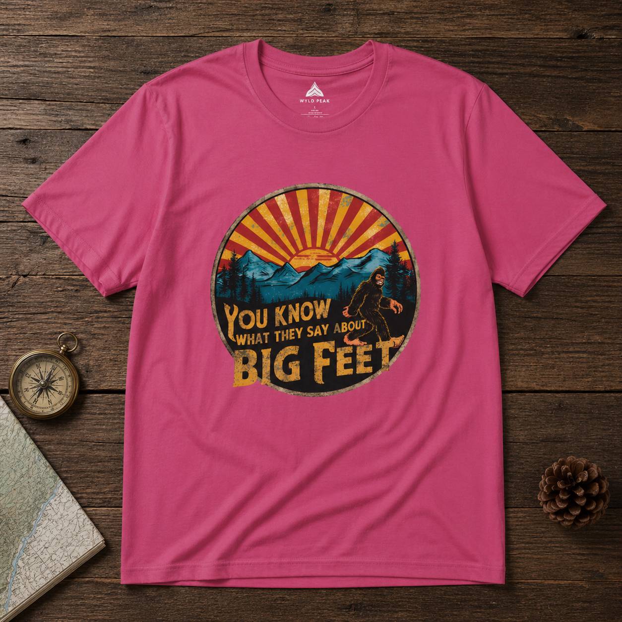 Pink t-shirt with a bigfoot graphic design on a wooden surface