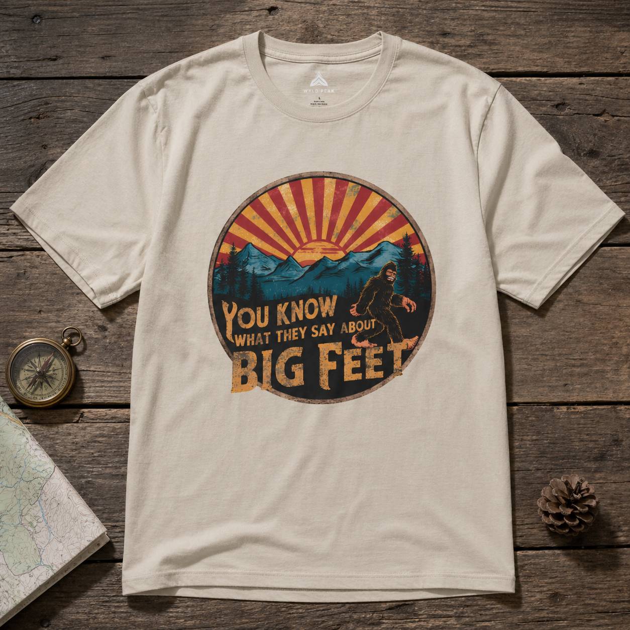 Beige t-shirt with a bigfoot graphic design on a wooden surface