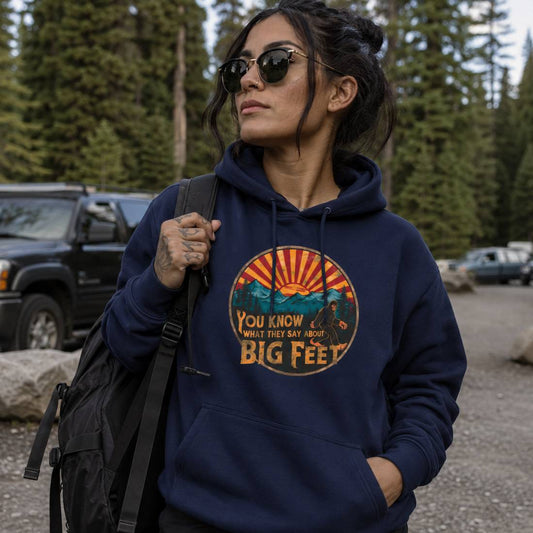 Person wearing a navy hoodie with a graphic design and text, standing outdoors with trees and a vehicle in the background.