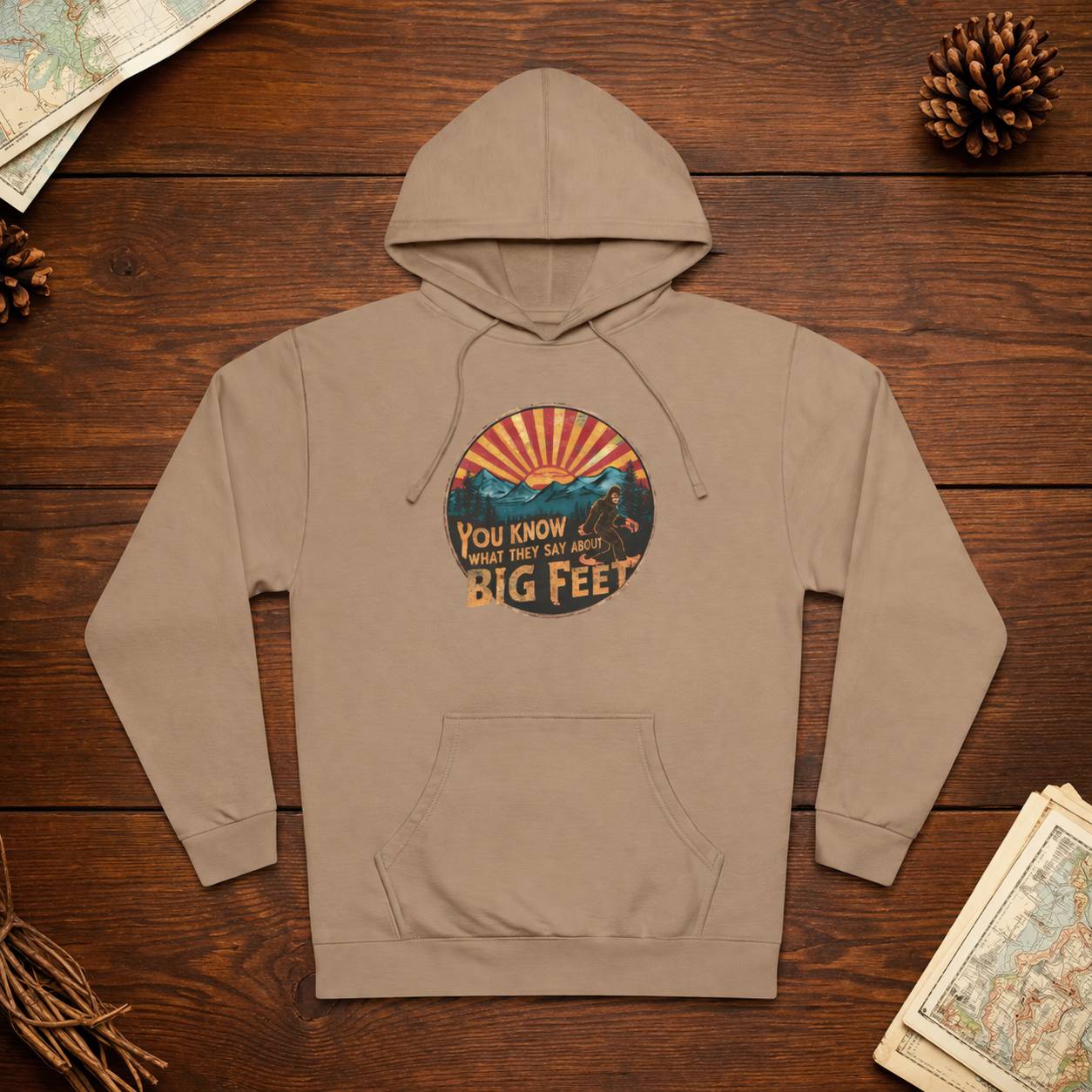 Beige hoodie with graphic design on a wooden surface with decorative items.