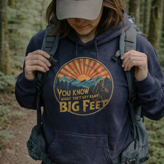 Person wearing a hoodie with a 'Big Feet' graphic in a forest setting