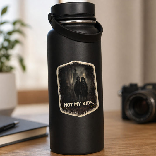Black water bottle with 'Not My Kids' label on a desk with a camera and notebook in the background