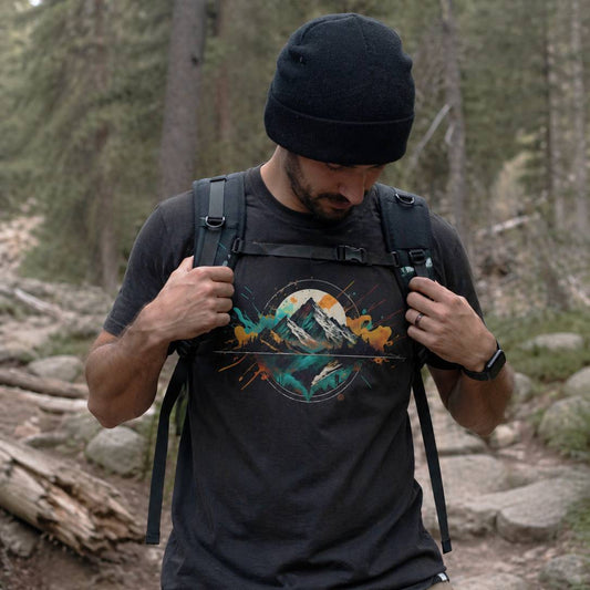 Man in a forest wearing a black t-shirt with a mountain design and a backpack.