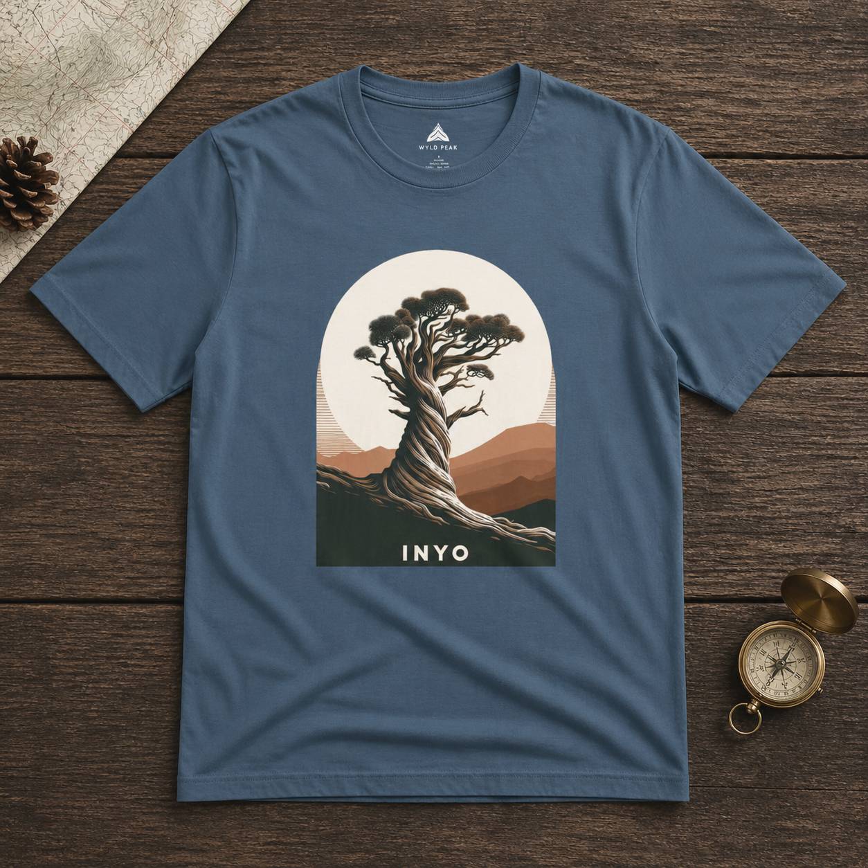 Blue t-shirt with a tree graphic and 'INYO' text on a wooden surface.