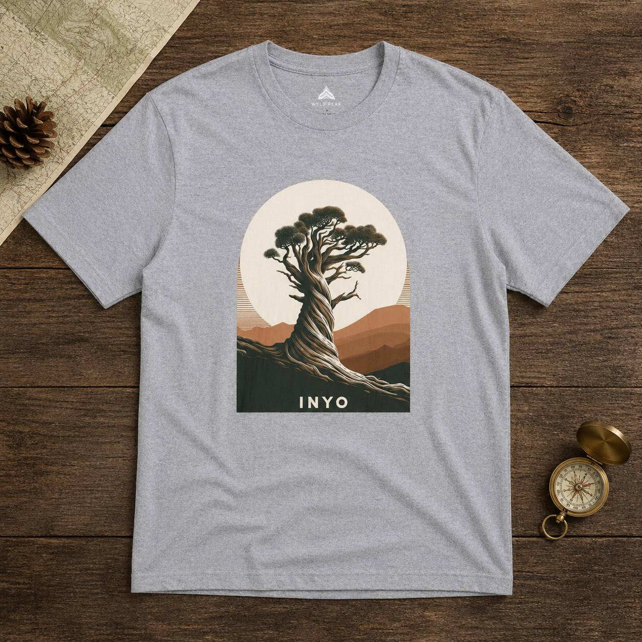 Gray t-shirt with a tree graphic and 'INYO' text on a wooden surface.