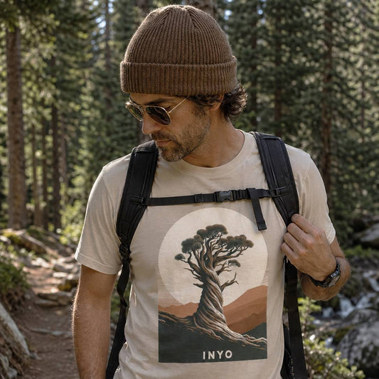 Man hiking in a forest wearing a t-shirt with a tree design and 'INYO' text.