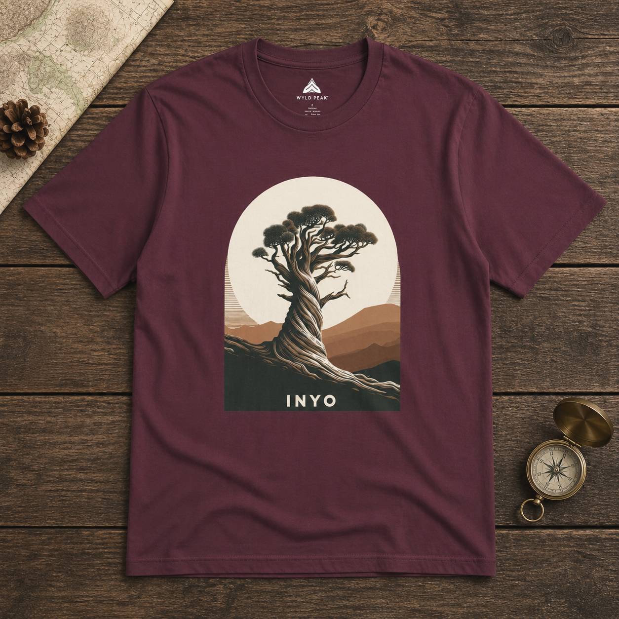 Maroon t-shirt with a tree graphic and 'INYO' text on a wooden surface.