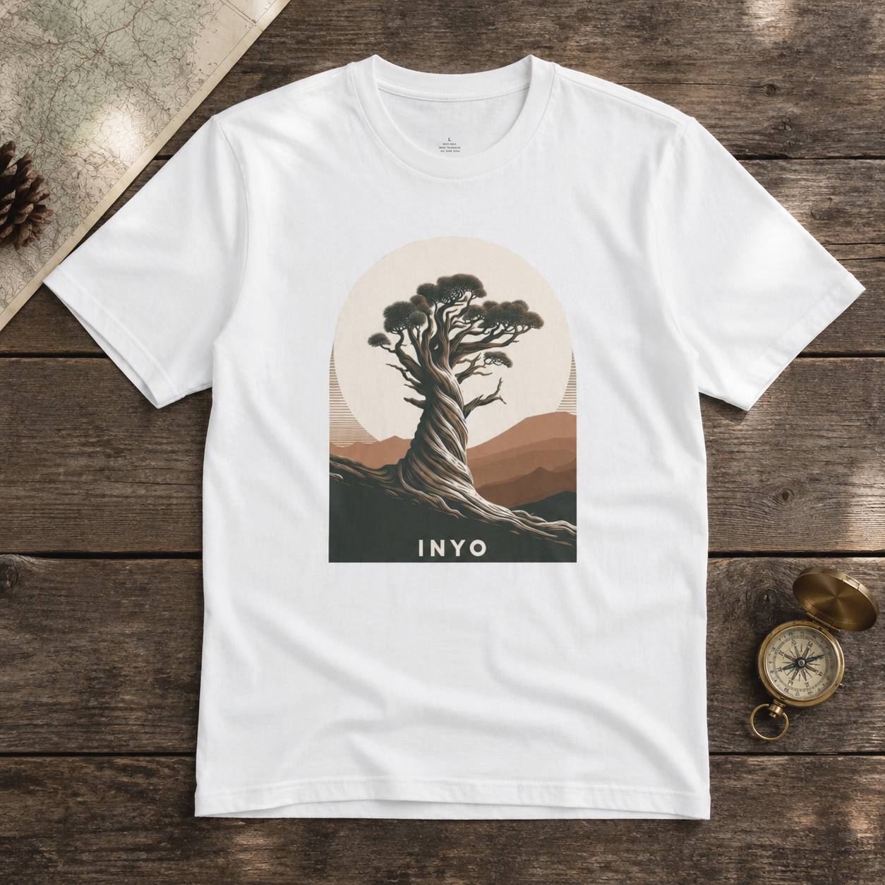 White t-shirt with a tree graphic and 'INYO' text on a wooden surface.