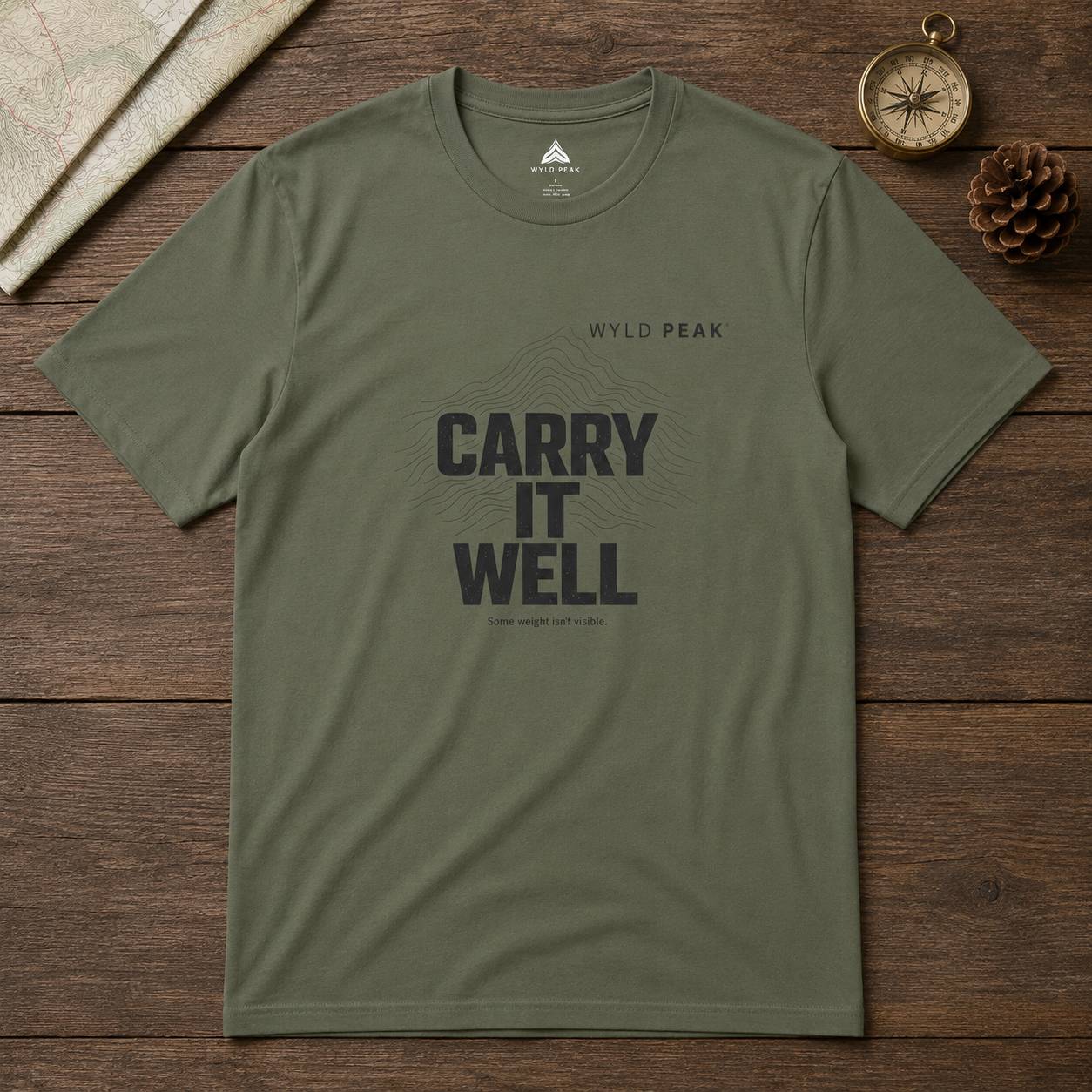 Green t-shirt with 'Carry It Well' text on a wooden surface