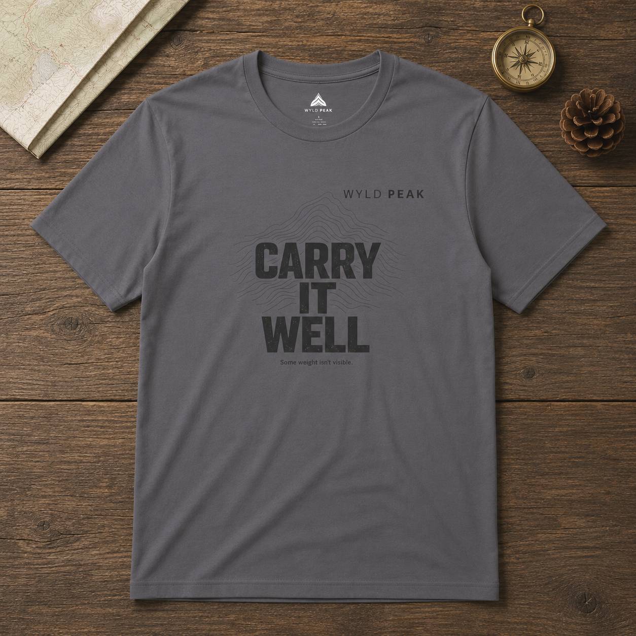 Gray t-shirt with 'CARRY IT WELL' text on a wooden surface