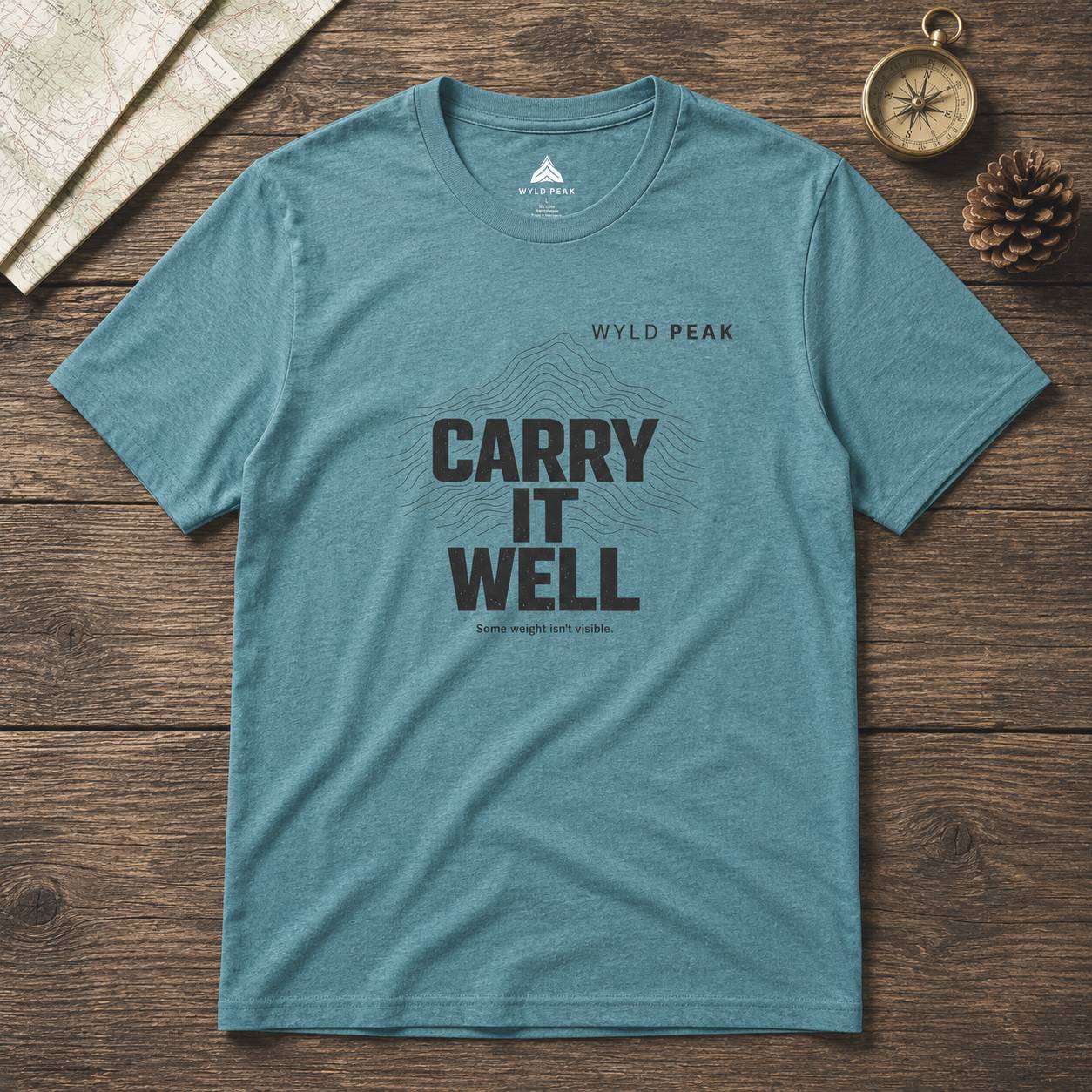 Blue t-shirt with 'Carry It Well' text on a wooden surface