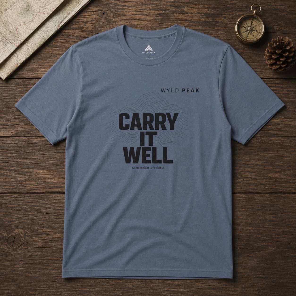 Blue t-shirt with 'Carry It Well' text on a wooden surface