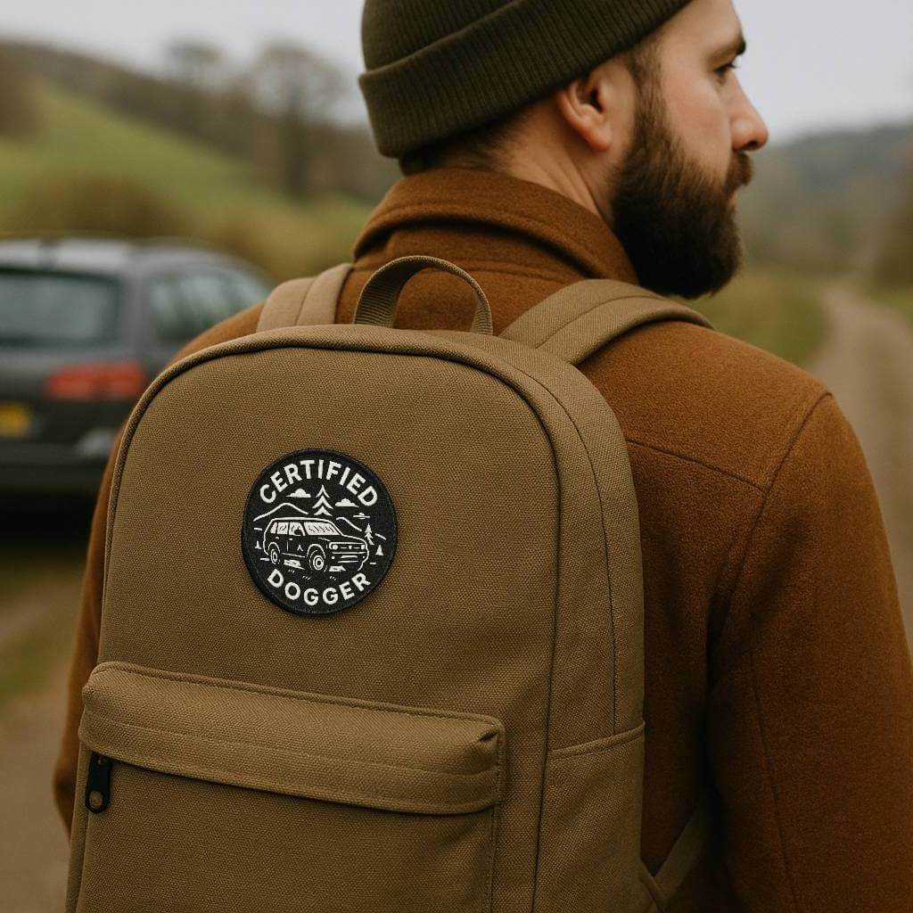 Wyld Peak Certified Dogger patch on a man's backpack in a back alley near a trail, with a fogged-up car in the background