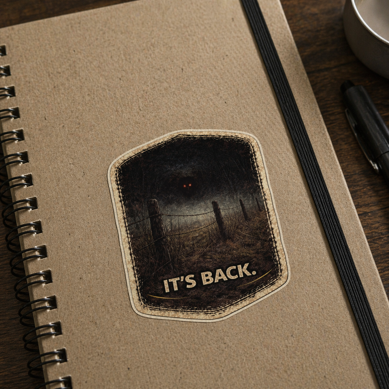 Notebook with a patch reading 'IT'S BACK.' on a wooden surface.