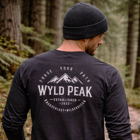 Man wearing a black long-sleeve shirt with 'Wyld Peak' logo in a forest setting