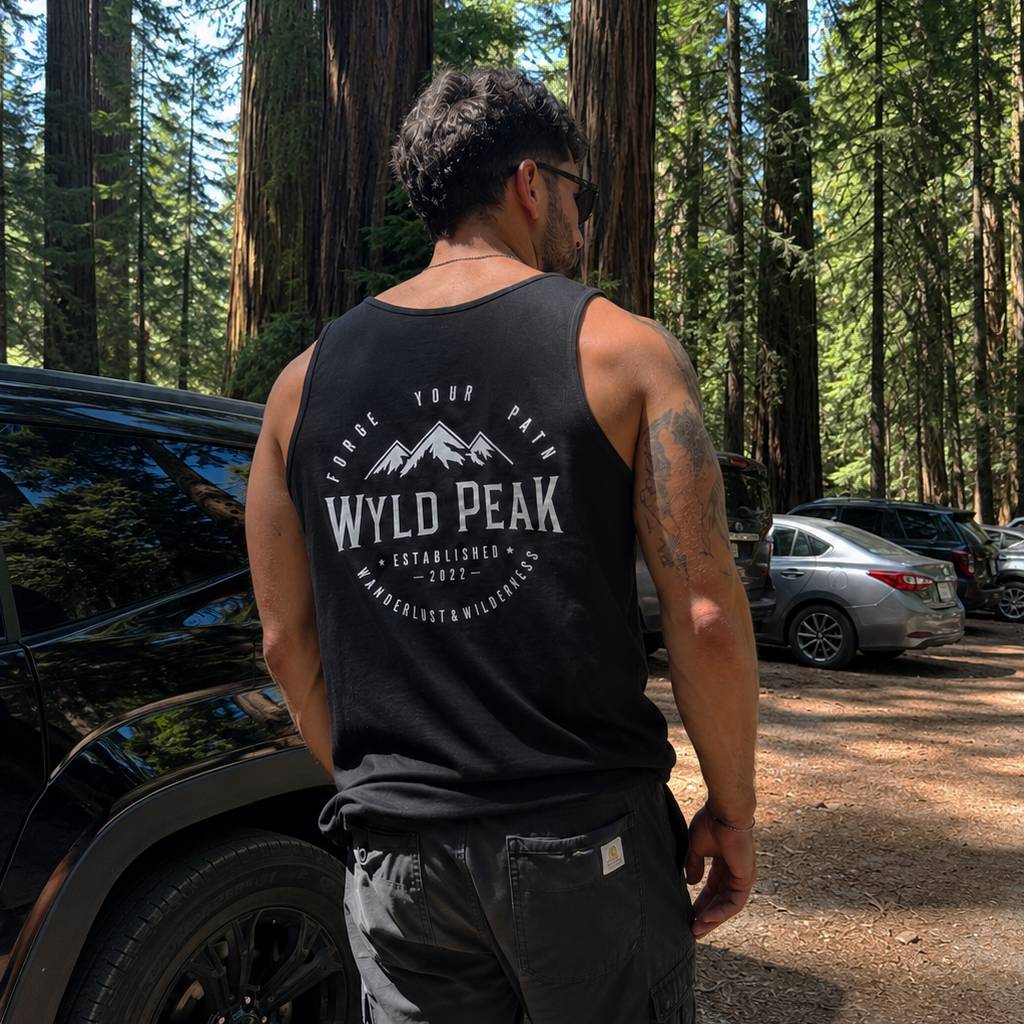 Person wearing a black tank top with 'Wyld Peak' logo in a forest setting