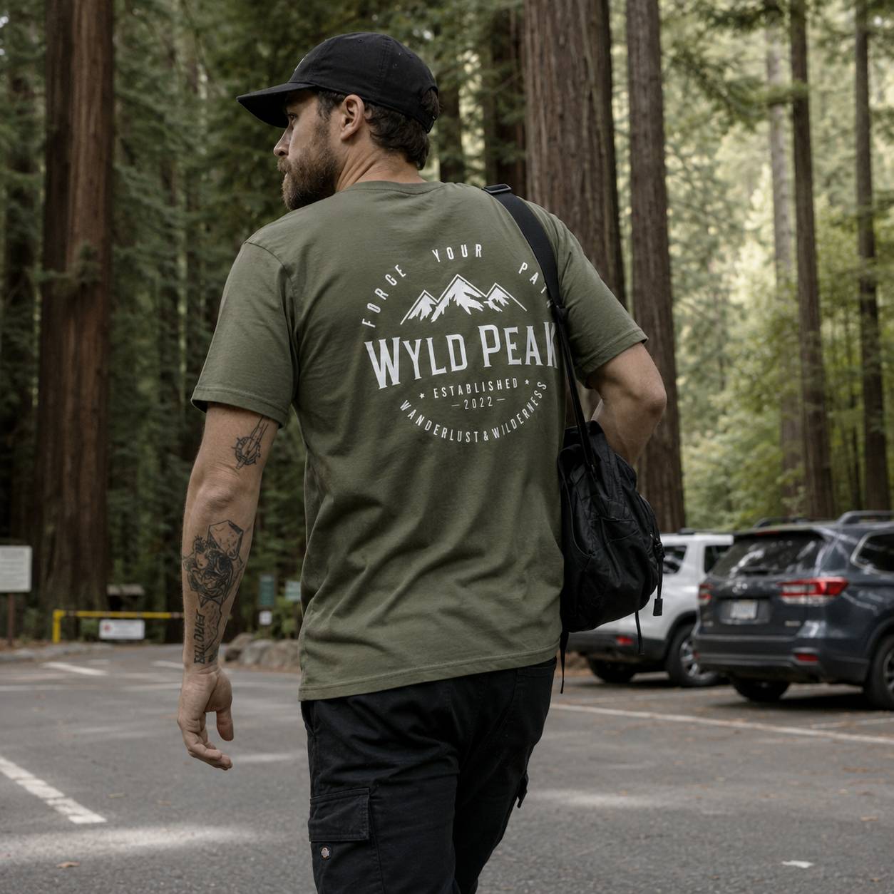 Man wearing a green t-shirt with 'Wyld Peak' branding in a forest setting